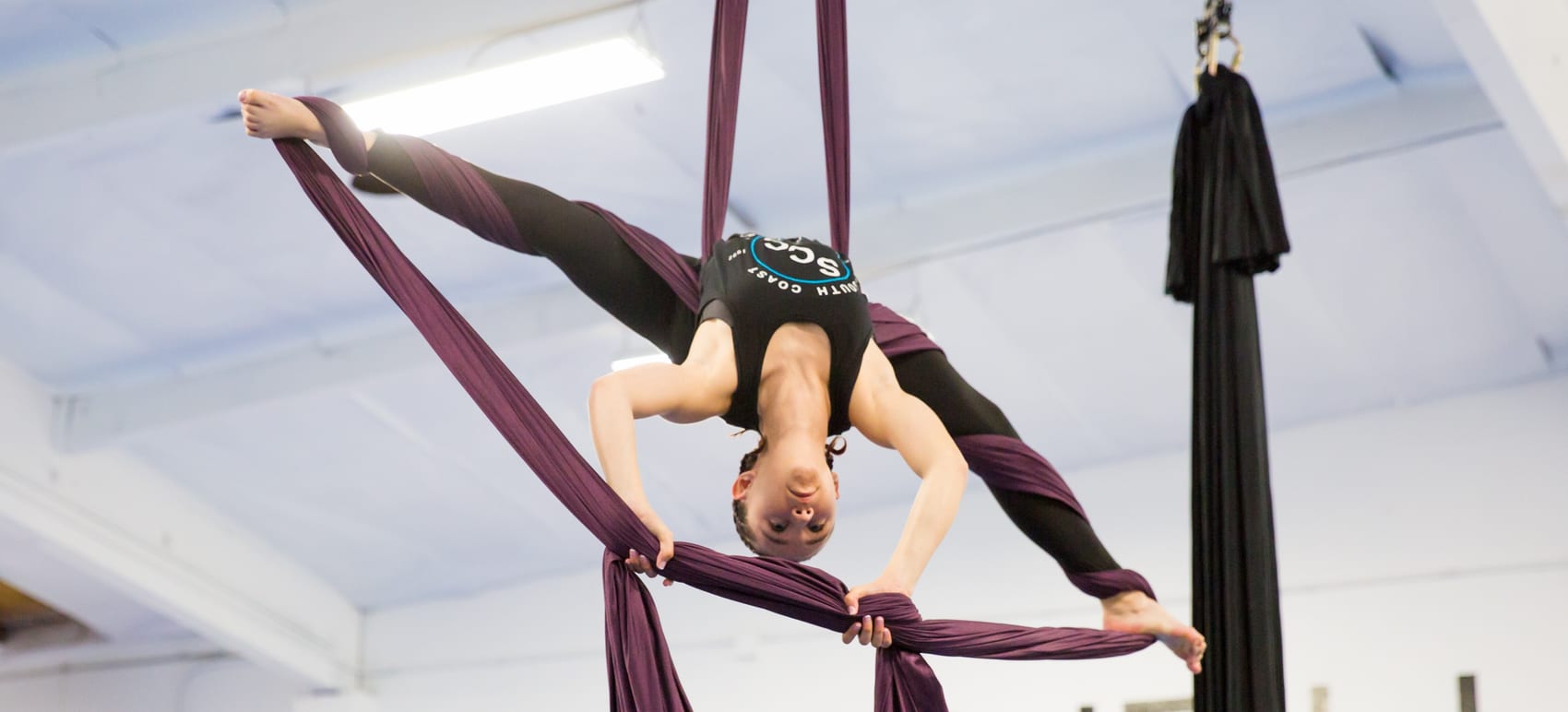An SCC dancer inverted in plum aerial silks in the studio’s Acro/Aerial gym
